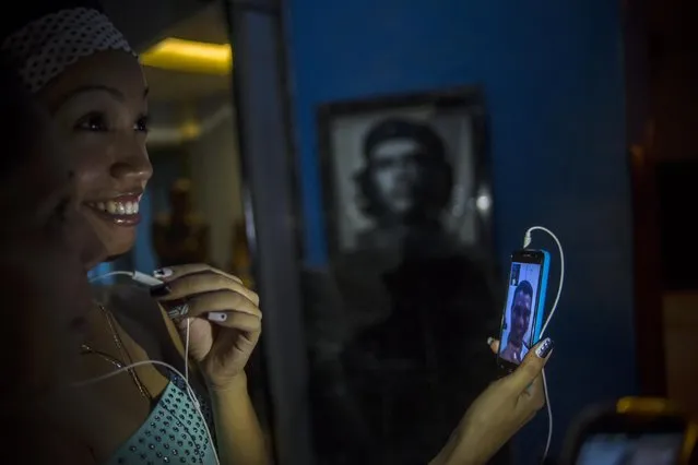 Two girls chat with a friend using a smartphone in a public Wi-Fi hotspot at the street in front of portrait of revolutionary leader Che Guevara in Havana, Friday, July 31, 2015. (Photo by Ramon Espinosa/AP Photo)
