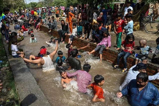 People cool themselves in a canal on a hot summer day in Lahore on May 15, 2022. (Photo by Arif Ali/AFP Photo)