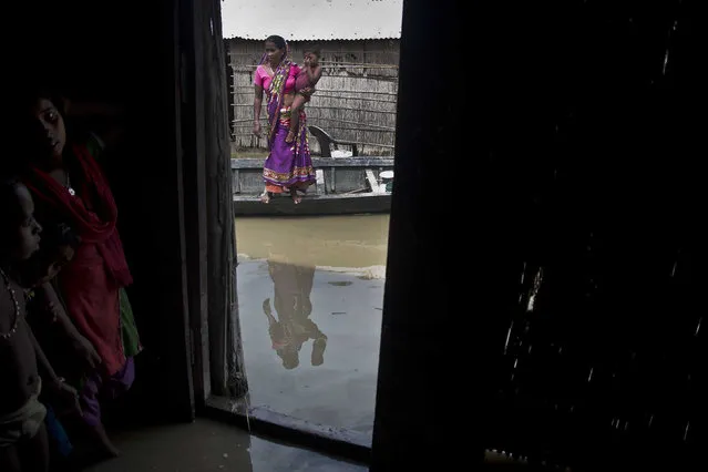 An Indian woman holding her child stands on a boat near their house partially submerged in flood waters in Burgaon, 80 kilometers (50 miles) east of Gauhati, Assam state, India, Wednesday, July 5, 2017. (Photo by Anupam Nath/AP Photo)