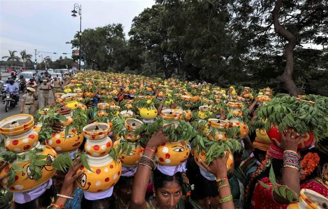 Hinudu women carry on their heads, pots filled with cooked rice decorated with turmeric and neem leaves as a ritual offering to the Hindu goddess Kali during the “Bonalu” festival in Hyderabad, India, Thursday, June 30, 2022. Bonalu is a month-long Hindu folk festival of the Telangana region dedicated to Kali, the Hindu goddess of destruction. (Photo by Mahesh Kumar A./AP Photo)