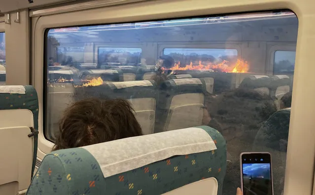 Passengers take photos at a wildfire while traveling on a train in Zamora, Spain, Monday, July 18, 2022. When Francisco Seoane's train unexpectedly stopped in Spanish countryside that was being engulfed by a wildfire, he and other passengers got a fright when they looked out at flames encroaching on both sides of the track. The Spaniard told The Associated Press it was scary to see how quickly the fire spread. Video of the unscheduled – and unnerving – stop shows about a dozen passengers in Seoane's railcar appearing alarmed as they look out of the windows Monday. (Photo by Francisco Seoane Perez/AP Photo)