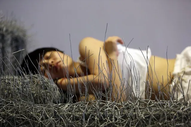 Chinese artist Zhou Jie takes a nap on an unfinished iron wire bed, one of her sculpture works, after lunch as a friend of hers looks on at Beijing Now Art Gallery, in Beijing August 11, 2014. Zhou started her art project titled “36 Days” on August 9, in which she would live inside an exhibition hall with an unfinished iron wire bed, some iron wire sculptures in the shape of stuffed animal dolls, a certain amount of food and her mobile phone, for 36 days. (Photo by Jason Lee/Reuters)