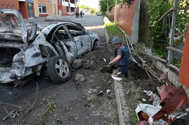 Deminers examine the site of a reported cluster munition fall after a rocket attack on a residential area in northern Kharkiv, on August 8, 2022, amid the Russian military invasion launched on Ukraine. The attack killed a resident and injured another. (Photo by Sergey Bobok/AFP Photo)