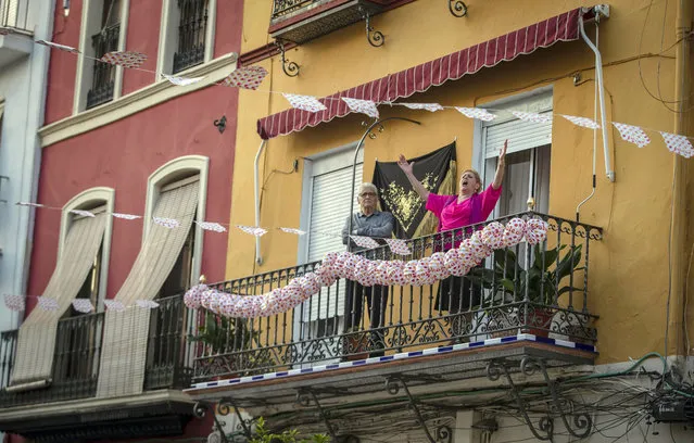 In this photo taken on Saturday April 25, 2020, a woman sings on her decorated balcony during the annual traditional April Fair in Seville, Spain. Without breaking the confinement rules and maintaining their distance from each other, the residents from their balconies, celebrated the tradition of the fair which has been cancelled due to the coronavirus outbreak and normally includes flamenco dancing, bullfighting, eating and drinking. (Photo by Miguel Morenatti/AP Photo)