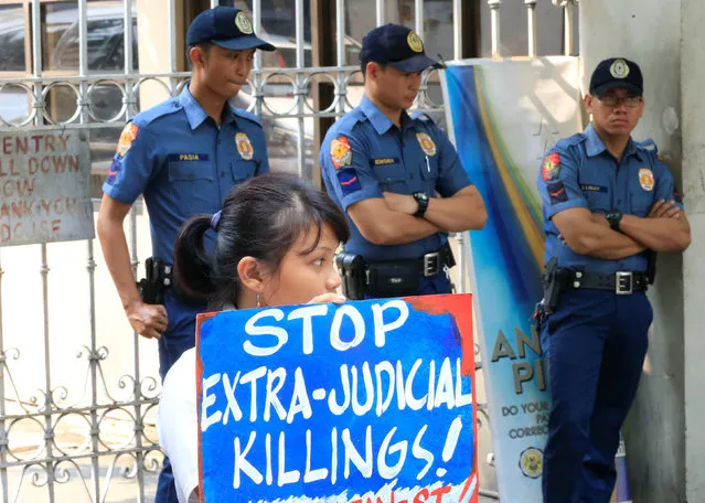 Anti-riot policemen stand guard in front of a protester holding a placard condemning the rise in extrajudicial killings in connection to the war on illegal drugs during a protest outside the Department of Justice in metro Manila, Philippines August 4, 2016. (Photo by Romeo Ranoco/Reuters)