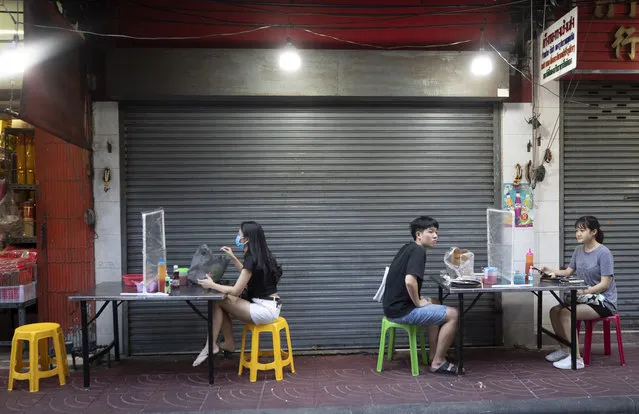 Customers wait on orders of street food from behind plastic sheets to help curb the spread of the coronavirus in Bangkok, Thailand, Tuesday, May 12, 2020. Small restaurants are one of the few businesses that have been allowed to open during an easing of restrictions in Thailand's capital Bangkok imposed weeks ago to combat the spread of the coronavirus. (Photo by Sakchai Lalit/AP Photo)
