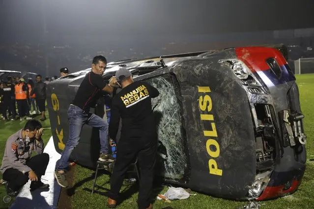 Officers examine a damaged police vehicle following a clash between supporters of two Indonesian soccer teams at Kanjuruhan Stadium in Malang, East Java, Indonesia, Saturday, October 1, 2022. Panic following police actions left over 100 dead, mostly trampled to death, police said Sunday. (Photo by Yudha Prabowo/AP Photo)