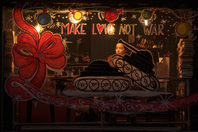 A woman sits in a pub with windows carrying holiday season wishes and an anti-war slogan in London, Monday, December 11, 2023. (Photo by Vadim Ghirda/AP Photo)