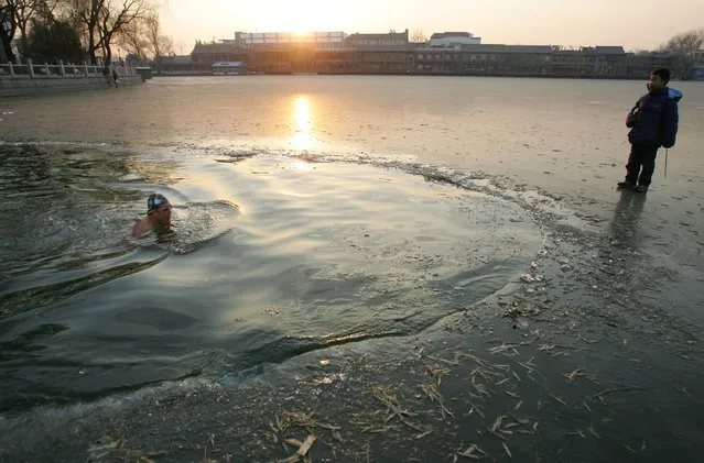 A man swims in the icy Shichahai Lake as a child looks on at a temperature around zero degrees centigrade December 17, 2006 in Beijing, China. Shichahai Lake is a popular place for swim enthusiasts in Beijing to go winter swimming. (Photo by China Photos)