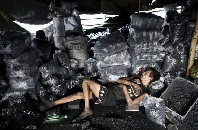 A worker rests next to bags of charcoal at a retailers repacking shop in Las Pinas, Metro Manila October 6, 2015. (Photo by Erik De Castro/Reuters)