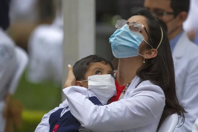 A health worker at the San Juan de Dios hospital holds a child during a minute of silence in memory of her colleagues who have fallen victim to COVID-19 in Guatemala City, Friday, October 9, 2020. (Photo by Moises Castillo/AP Photo)