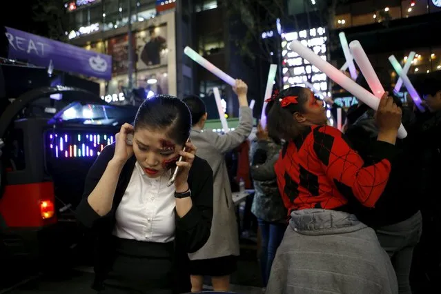 A woman wearing Halloween face paint talks on the phone among the others participating in a dance performance during Halloween celebrations in the downtown of Seoul, South Korea, October 31, 2015. (Photo by Kim Hong-Ji/Reuters)