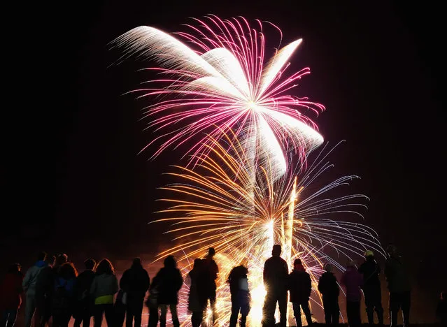 Hundreds of people stand on nearby cliffs as fireworks expode in the night sky as they attend the annual bonfire and fireworks display on November 5, 2015 in Skinningrove, England. The theme this year for this popular display is the fishing heritage of Skinningrove. A huge wooden fishing boat was built by the local community over the days leading up to the bonfire using donated wood and it formed the main focus of the display. (Photo by Ian Forsyth/Getty Images)