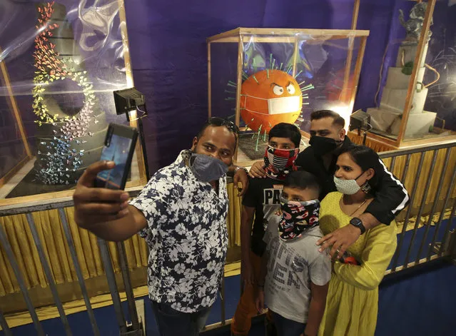 Members of a family wearing face masks take a selfie with a cake depicting the coronavirus on display at the annual cake show organized as part of New Year celebrations in Bengaluru, India, Tuesday, December 29, 2020. India's confirmed coronavirus cases have crossed 10 million with new infections dipping to their lowest levels in three months, as the country prepares for a massive COVID-19 vaccination in the new year. (Photo by Aijaz Rahi/AP Photo)