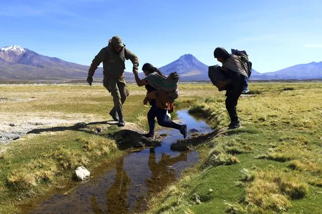 A Chilean soldier helps a migrant cross a water canal near Colchane, Chile, Wednesday, March 1, 2023, before the migrants are taken to a shelter where police register them. The government announced it's increasing military presence on its border with Peru and Bolivia to tackle illegal immigration. (Photo by Ignacio Munoz/AP Photo)