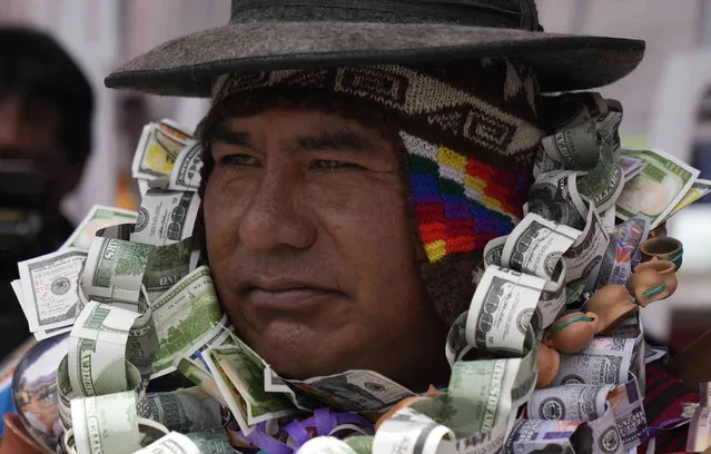 A person dressed as an Ekeko, the God of prosperity, is covered in fake money on the opening day of the annual Alasita Fair, where the Ekeko is its central figure in El Alto, Bolivia, Tuesday, January 24, 2023. People buy tiny replicas of things they aspire to acquire during the year, like homes, cars and wealth. The Aymara word “Alasita“ means “buy me”. (Photo by Juan Karita/AP Photo)