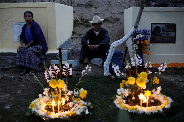 Residents sit next to the decorated tombs of their loved one during the commemoration of All Saints Day at a cemetery in Sacatepequez, Guatemala, November 1, 2016. (Photo by Luis Echeverria/Reuters)