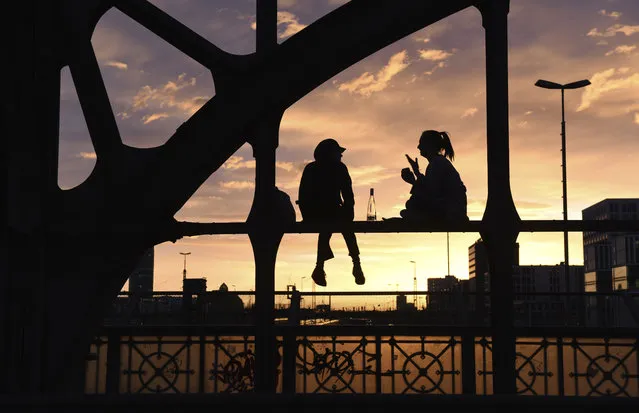 Two women are silhouetted against the setting sun as they sit on a steel beam of a bridge in Munich, southern Germany, Thursday, April 12, 2018. (Photo by Tobias Hase/DPA via AP Photo)