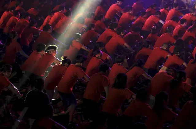 A participant is seen under a beam of light as hundreds of people ride indoor bicycles during a campaign to promote body-building exercises, at a gymnasium in Kunming, Yunnan province, China, December 1, 2015. (Photo by Wong Campion/Reuters)