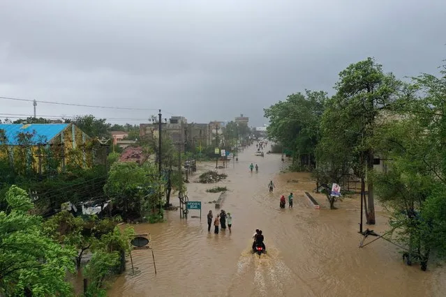 An aerial picture shows residents wading along a waterlogged road in Mandvi on June 16, 2023, after Cyclone Biparjoy made landfall. Cyclone Biparjoy tore down power poles and uprooted trees Friday after pummelling the Indian coastline, though the storm was weaker than feared and there were no immediate reports of deaths. (Photo by Shubham Koul/AFP Photo)