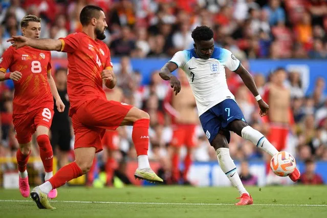 England's midfielder Bukayo Saka (R) shoots past North Macedonia's defender Gjoko Zajkov to score their fourth goal during the UEFA Euro 2024 group C qualification football match between England and North Macedonia at Old Trafford in Manchester, north west England, on June 19, 2023. (Photo by Oli Scarff/AFP Photo)