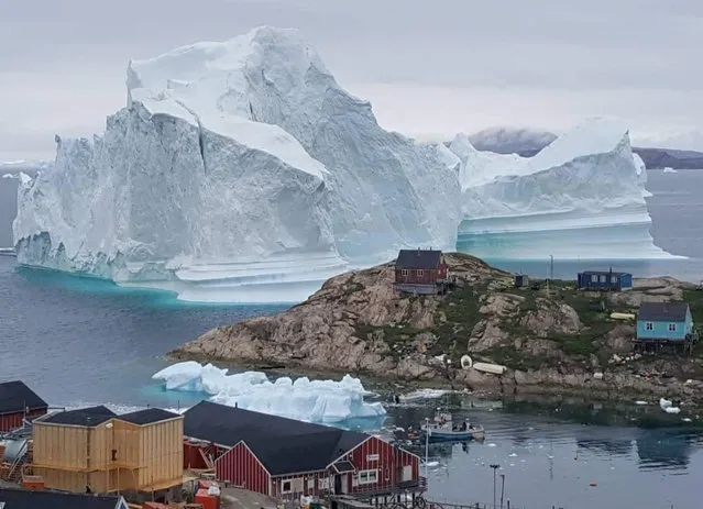 A giant iceberg is seen behind an Innaarsuit settlement, Greenland July 12, 2018. Scientists have watched an iceberg four miles long break off from a glacier. The iceberg is allegedly grounded on the sea floor. Residents in houses near the shore are prepared for an evacuation. (Photo by Karl Petersen/Reuters/Ritzau Scanpix)