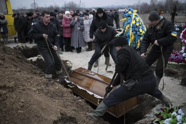 Municipal workers place a coffin with a body of Alexander Demyanenko, victim of Saturday shelling into the graved during funerals in Mariupol, Ukraine, on Monday January 26, 2015. (Photo by Evgeniy Maloletka/AP Photo)