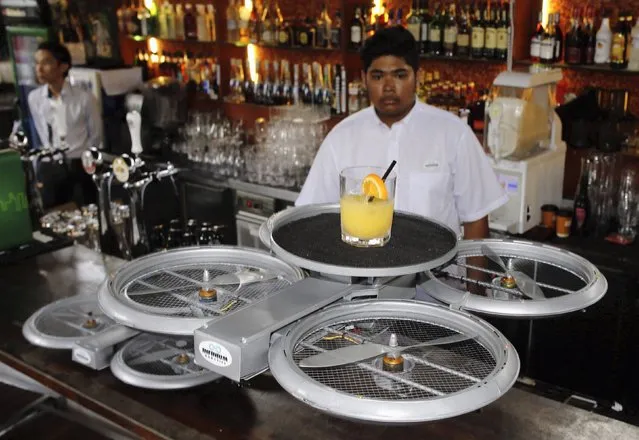 A bartender watches as an Infinium-Serve Flying Robot takes off with an order at a restaurant during a pilot demonstration for the media in Singapore February 5, 2015. The Unmanned Aerial Vehicle (UAV), a working model designed by firm Infinium Robotics that specializes in UAV solutions, aims to free up restaurant staff to do “higher value tasks” by accurately delivering orders up to 500 grams to tables within the premise by means of anti-collision algorithms, according to Chief Executive Officer Woon Junyang. (Photo by Edgar Su/Reuters)