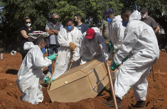 Cemetery workers in full protective gear lower a coffin that contain the remains of a person who died from complications related to COVID-19 at the Vila Formosa cemetery in Sao Paulo, Brazil, Wednesday, March 24, 2021. (Photo by Andre Penner/AP Photo)