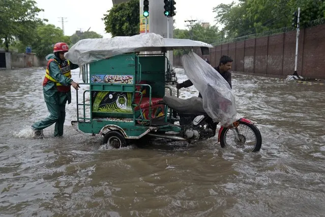 A rescue worker helps a driver pushing his motorcycle rickshaw through a flooded road caused by heavy monsoon rainfall in Lahore, Pakistan, Wednesday, July 5, 2023. Officials say heavy monsoon rains have lashed across Pakistan, killing a number of people. (Photo by K.M. Chaudary/AP Photo)