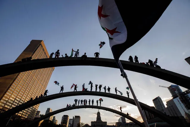 Demonstrators wave flags atop the arches of Toronto City Hall as thousands gather in Toronto, Ontario, Canada to show their support for the people of Palestine, on May 15, 2021. Pro-Palestinian demonstrators rallied in cities across North America on Saturday, calling for an end to Israeli attacks on the Gaza Strip as the worst violence in years flared between the Jewish state and Islamist militants. (Photo by Cole Burston/AFP Photo)