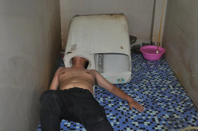 A man lies on the floor with his head stuck in a washing machine in Fuzhou, China May 29, 2016. According to local media, the man was trying to figure out why the machine was not working when his head became trapped. Firefighters eventually cut the machine and saved him. (Photo by Reuters/Stringer)