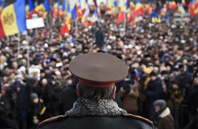 A Moldovan army general watches demonstrators during a large protest in Chisinau, Moldova, Sunday, January 24, 2016. More than 15,000 people gathered to protest against the government, demanding early elections in the impoverished East European nation, an action that comes after demonstrators stormed Parliament last week as lawmakers approved a new pro-European government. (Photo by Vadim Ghirda/AP Photo)