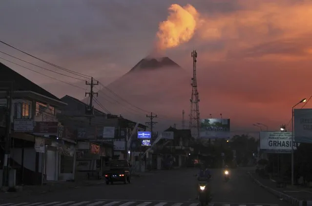 Motorists ride past as Mount Merapi looms in the background, in Sleman, Friday, June 25, 2021. Indonesia’s most volatile volcano erupted Friday, releasing plumes of ash high into the air and sending streams of lava with searing gas clouds flowing down its slopes. (Photo by Slamet Riyadi/AP Photo)