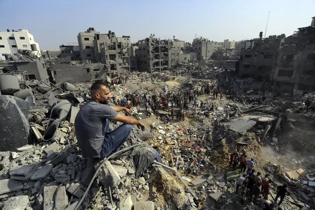 A man sits on the rubble as others wander among debris of buildings that were targeted by Israeli airstrikes in Jabaliya refugee camp, northern Gaza Strip, Wednesday, November 1, 2023. (Photo by Abed Khaled/AP Photo)
