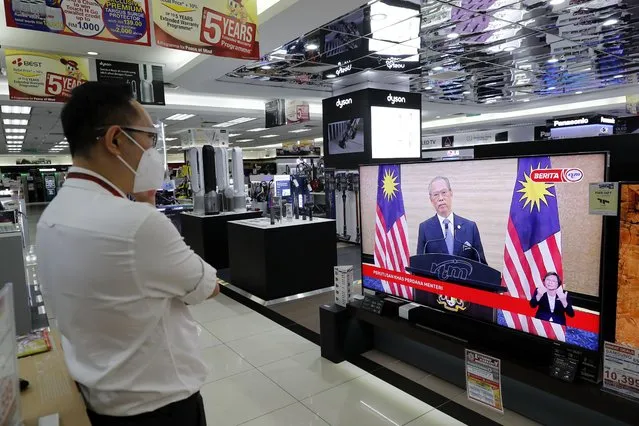An electronic shop staff wearing a face mask watches live broadcast of Malaysian Prime Minister Muhyiddin Yassin speak at a shopping outlet in Kuala Lumpur, Malaysia, Monday, August 16, 2021. Muhyiddin resigned less than 18 months into his tenure Monday, becoming the country's shortest-ruling leader after conceding that he lost majority support to govern. (Photo by F.L. Wong/AP Photo)