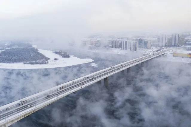 An aerial view of cars passing through the Oktyabrsky Bridge while steam rises from the Yenisei River during –30 Celsius degrees as the water evaporates rather than freezing even in severe frosts during winter due to the design of Krasnoyarsk hydroelectric power station, located 50 km upstream of the river in Krasnoyarsk, Russia on December 8, 2023. (Photo by Aleksander Manzyuk/Anadolu via Getty Images)