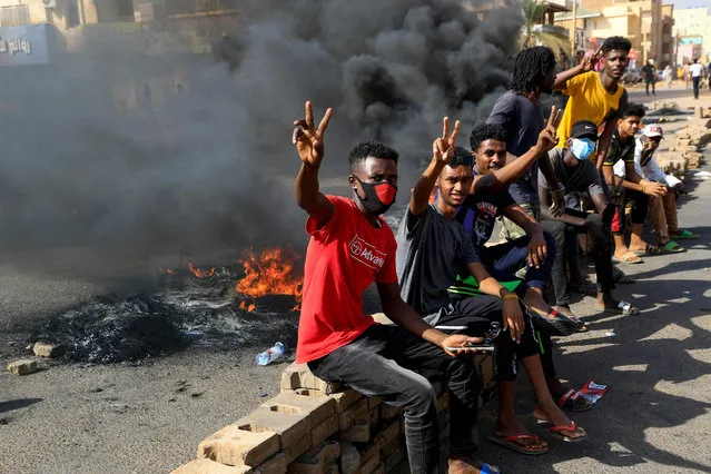 Sudanese protesters flash the V for victory sign as they burn tyres to block a road in 60th Street in the capital Khartoum, to denounce overnight detentions by the army of members of Sudan's government, on October 25, 2021. Armed forces detained Sudan's Prime Minister over his refusal to support their “coup”, the information ministry said, after weeks of tensions between military and civilian figures who shared power since the ouster of autocrat Omar al-Bashir. (Photo by AFP Photo/Stringer)
