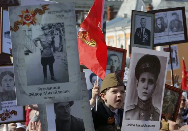 A boy waves a flag from behind portraits of World War Two soldiers during the Immortal Regiment march on Red Square as part of the Victory Day celebrations in Moscow, Russia, May 9, 2015. (Photo by Maxim Shemetov/Reuters)
