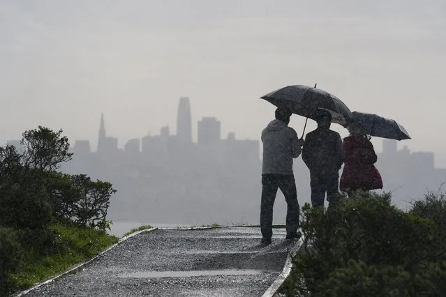 People walk in the rain near Sausalito, Calif., with the San Francisco skyline in the background Monday, February 5, 2024. In Northern California, the storm inundated streets and brought down trees and electrical lines Sunday throughout the San Francisco Bay Area, where winds topped 60 mph (96 kph) in some areas. (Photo by Eric Risberg/AP Photo)