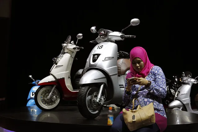 A woman uses her smartphone beside Peugeot scooter at the Indonesian International Motor Show in Jakarta, Indonesia, April 7, 2016. (Photo by Reuters/Beawiharta)