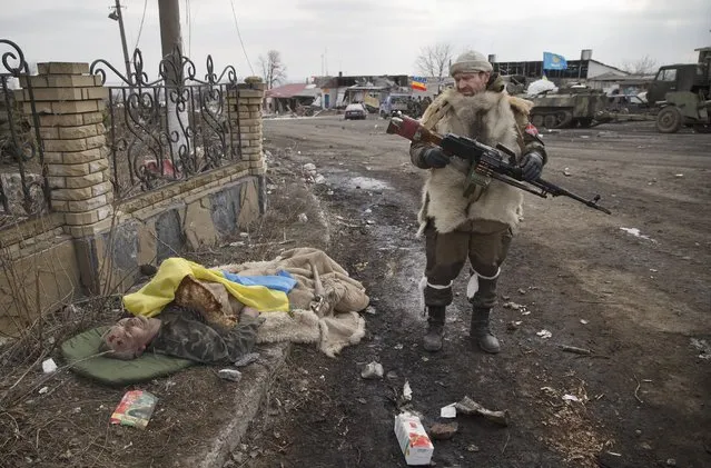 A Russia-backed rebel looks at the flag covered body of an Ukrainian serviceman in Debaltseve, Ukraine, February 20, 2015. The struggle for the strategic rail hub, Debaltseve, a sleepy town with a pre-war population of 25,000 people, left the town in ruins and became one of the darkest pages in the ongoing conflict in eastern Ukraine, which has already killed more than 6,000 people. (Photo by Vadim Ghirda/AP Photo/File)