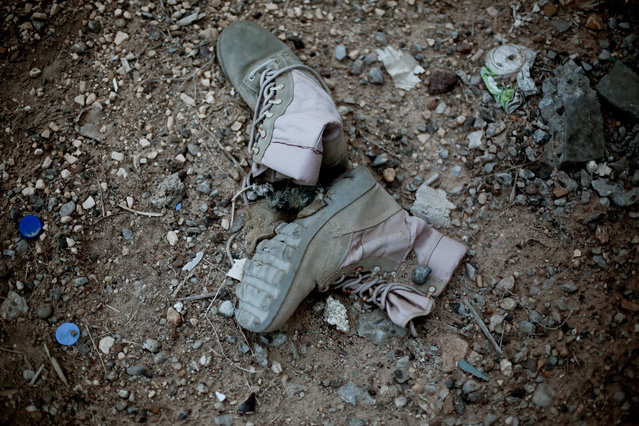 Combat boots lie in the dirt on March 20, 2016, in Ramadi, left behind after a battle weeks earlier between Islamic State group militants and Iraqi security forces. As they fled Ramadi earlier this year, the militants destroyed some buildings and booby-trapped others with explosives in a scorched earth tactic that left behind an empty prize for government forces retaking the city. (Photo by Maya Alleruzzo/AP Photo)