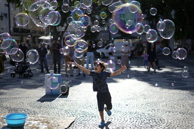 A child runs after soap bubbles being made by a street artist at Lisbon's downtown Rossio square, Friday, September 16, 2022. (Photo by Armando Franca/AP Photo)