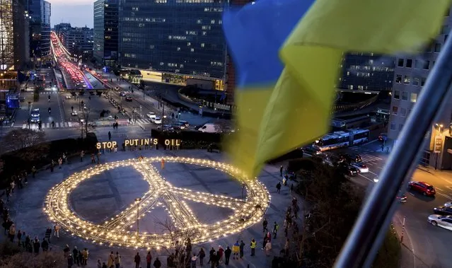 People stand around a giant peace sign with the message “Stop Putin's Oil”, put up by demonstrators ahead of an EU and NATO summit in Brussels, Tuesday, March 22, 2022. Protestors on Tuesday called on EU leaders to impose a full ban on Russian fuels and to hold one minute of silence to honor the victims of war. (Photo by Geert Vanden Wijngaert/AP Photo)
