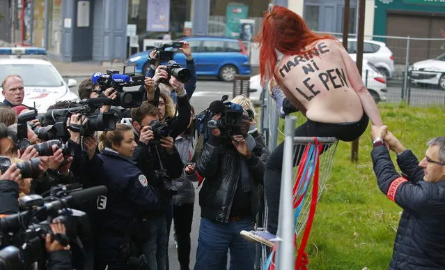 A Femen activist is led away by police after activists lowered a banner protesting against Marine Le Pen's FN party in Henin-beaumont, northern France, Sunday, May 7, 2017. Voters across France are choosing a new president in an unusually tense and important election that could decide Europe's future, making a stark choice between pro-business progressive candidate Emmanuel Macron and far-right populist Marine Le Pen. The text on the activists' back reads “Neither Marine Nor Le Pen”. (Photo by Michel Spingler/AP Photo)