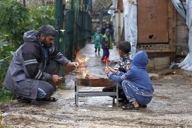A displaced Syrian family warms themselves around a fire at a refugee camp in the southern port city of Sidon, Lebanon, Wednesday, January 19, 2022. A snowstorm in the Middle East has left many Lebanese and Syrians scrambling to find ways to survive. Some are burning old clothes, plastic and other hazardous materials to keep warm as temperatures plummet and poverty soars. (Photo by Mohammed Zaatari/AP Photo)