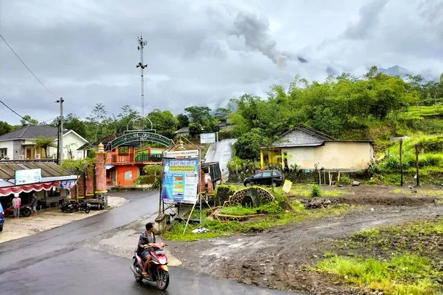 A man rides a motorcycle past a street with Mount Merapi covered in fog in the background, seen from Cangkringan village in Sleman, Yogyakarta, Thursday, March 10, 2022. Indonesia's Mount Merapi volcano spewed avalanches of hot clouds in eruptions overnight Thursday that forced about 250 residents to flee to temporary shelters. No casualties were reported. (Photo by Slamet Riyadi/AP Photo)