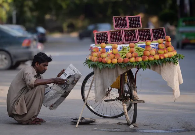 A Pakistani fruit vendor reads a newspaper as he waits for customers on a street in Islamabad on May 23, 2017. (Photo by Aamir Qureshi/AFP Photo)