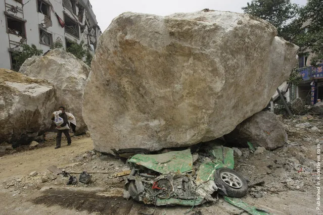 A survivor carrying goods evacuates the area past a huge rock lying on top of a car on a road near a mountain in the centre of earthquake-hit Beichuan county, Sichuan province, May 16, 2008